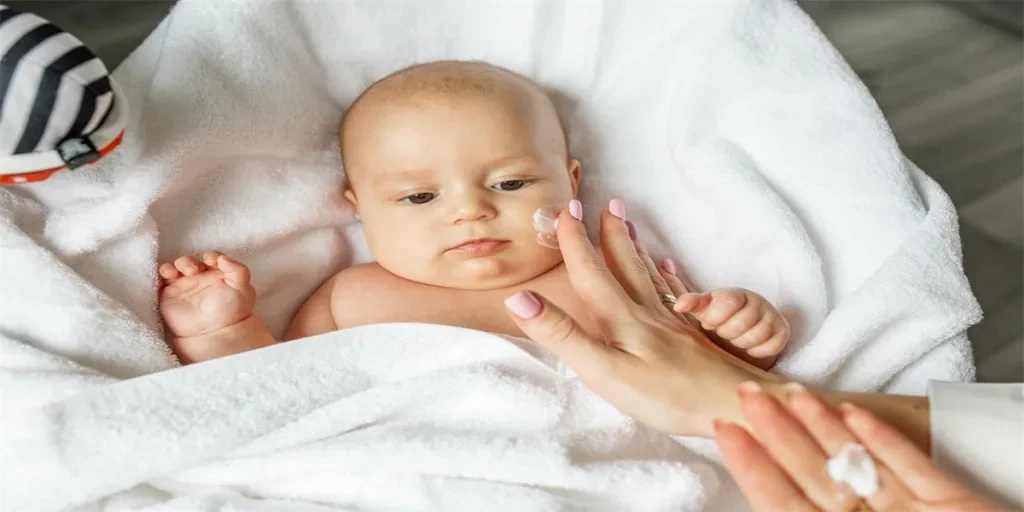 Mother applies moisturizer for healthy skin care on cute baby face