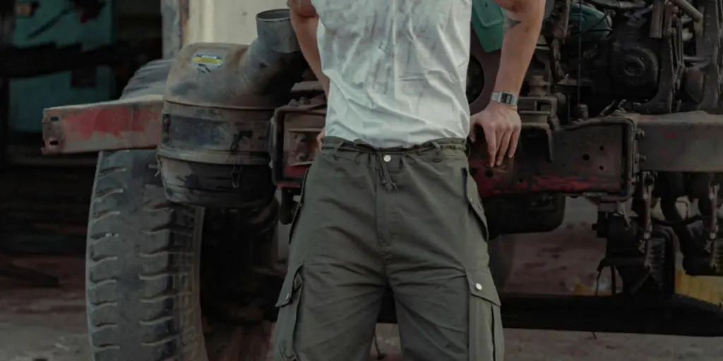 Muscular man with beard and mustache standing confidently in a garage workshop beside a rusty vehicle 