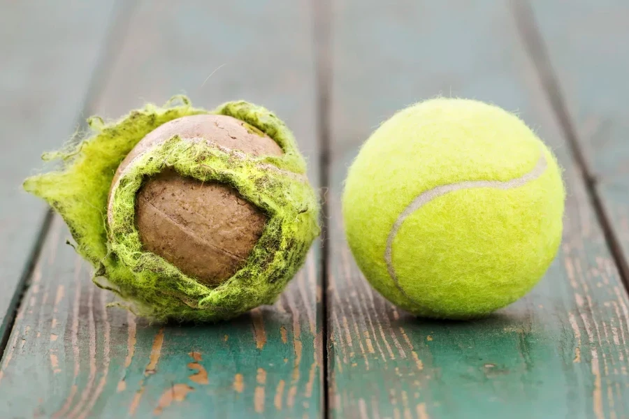 Old used dirty and new yellow tennis balls on green wooden background