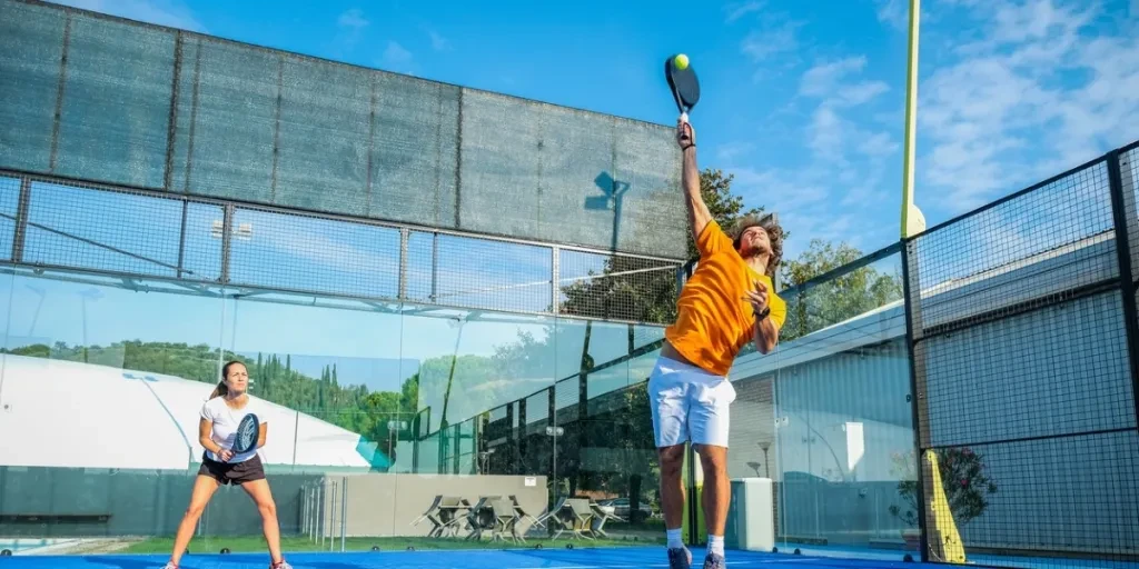 Paddle tennis player making an effort to while hitting the ball during a match on outdoor court.