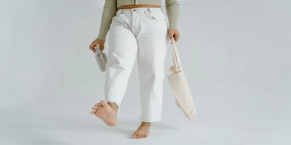 Person walking barefoot with reusable cloth bag and water bottle, promoting zero waste lifestyle by Tima Miroshnichenko