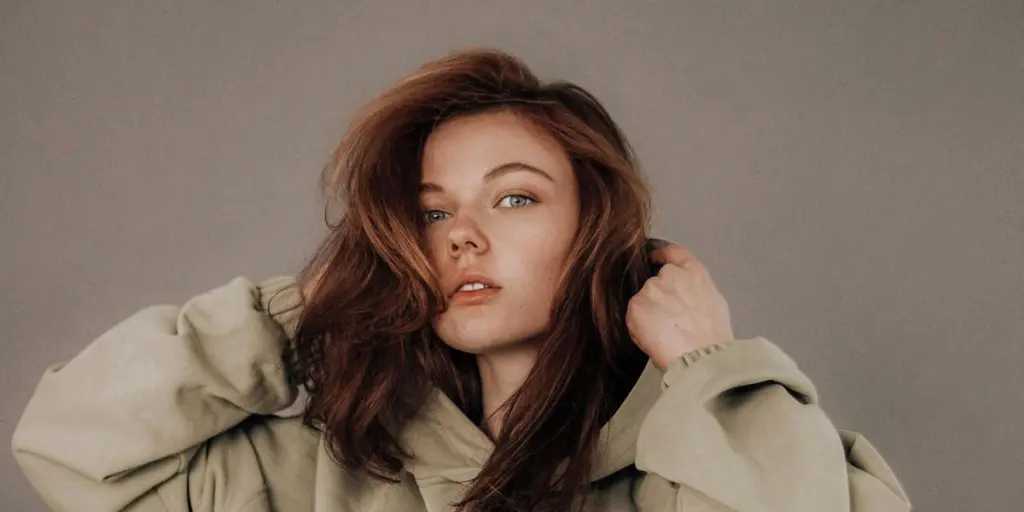 Portrait of a confident young woman in a trendy beige hoodie against a gray background