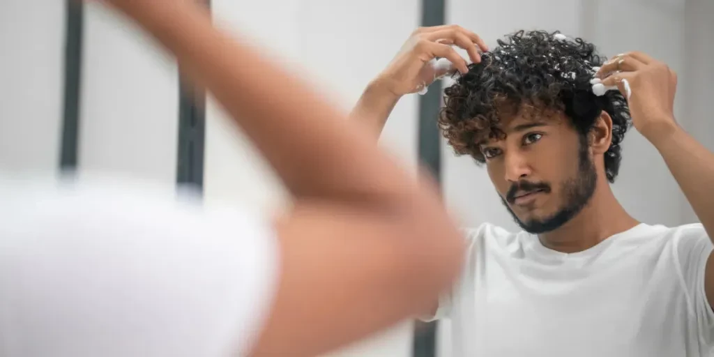 Portrait of a serious young Indian man applying the foaming mousse to his curly hair