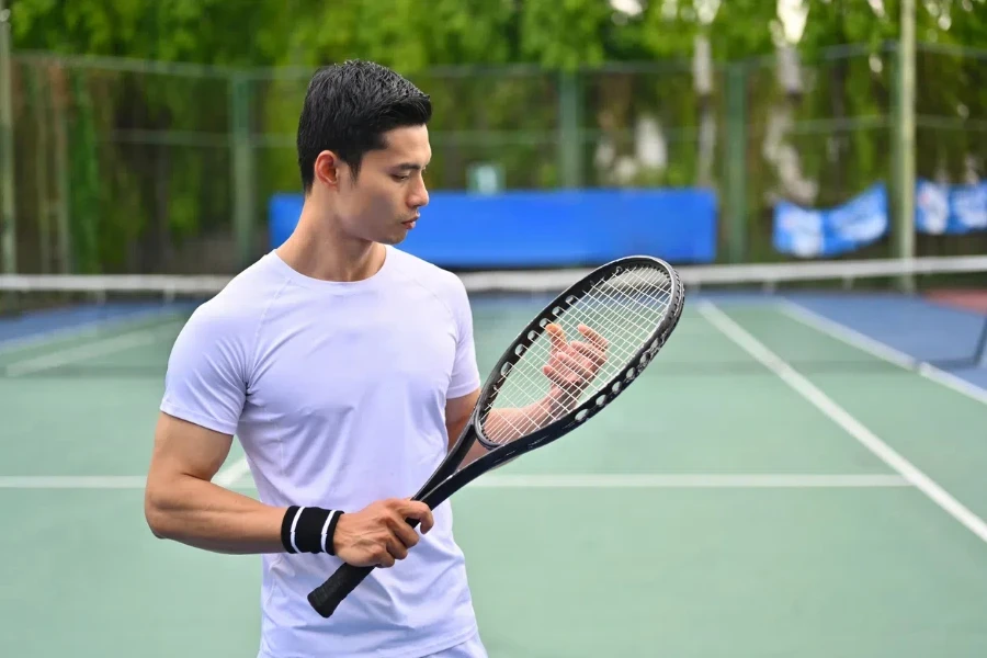 Potret pemain tenis pria Asia dengan raket berdiri di lapangan pada hari yang cerah