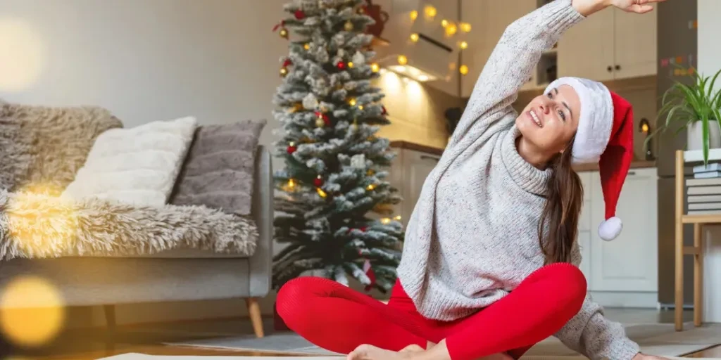 Positive woman wearing a Santa hat doing yoga on an exercise mat at home during the Christmas holidays