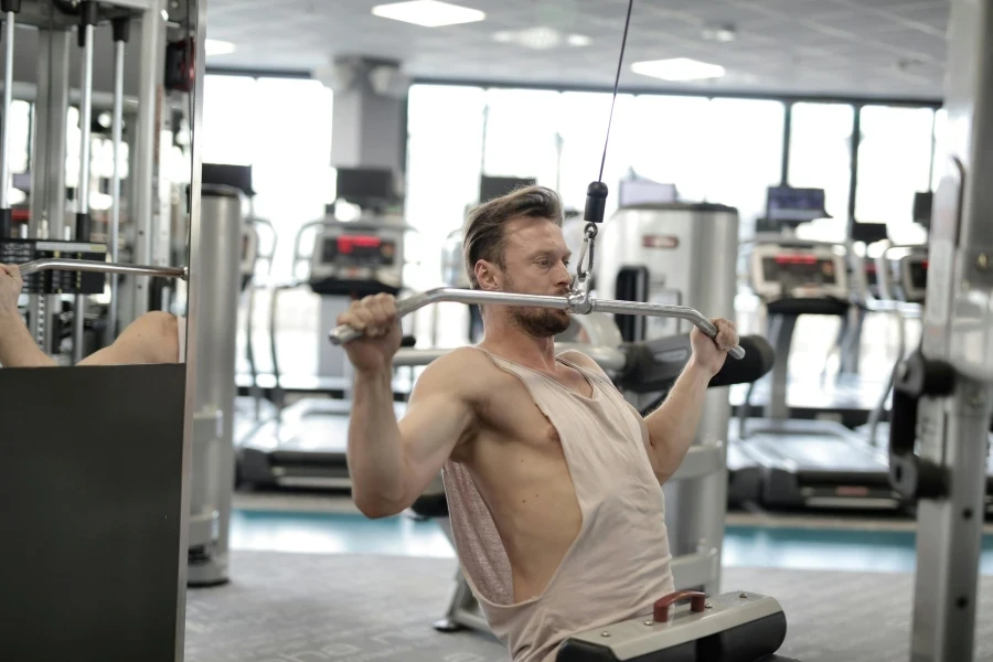 Powerful muscular male athlete in casual sportswear performing exercise with metal bar on machine while training hard in modern fitness club