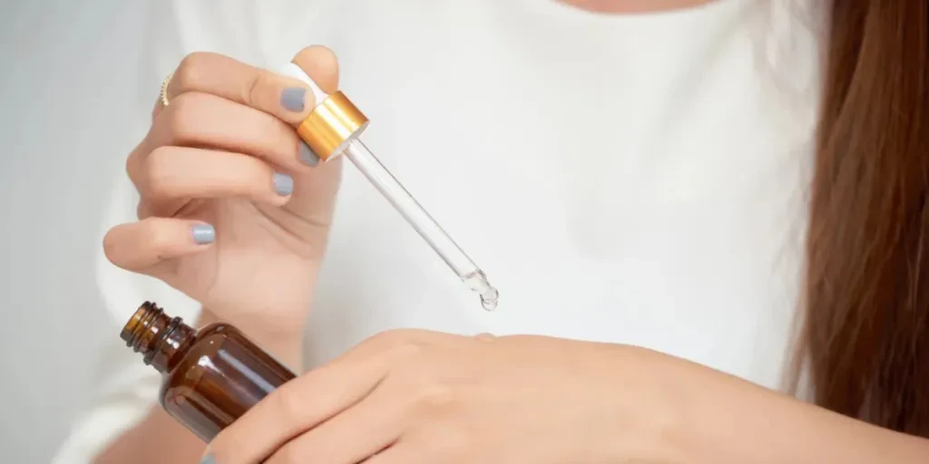 Pretty Caucasian woman putting cosmetic serum on her hand while sitting at the dressing table