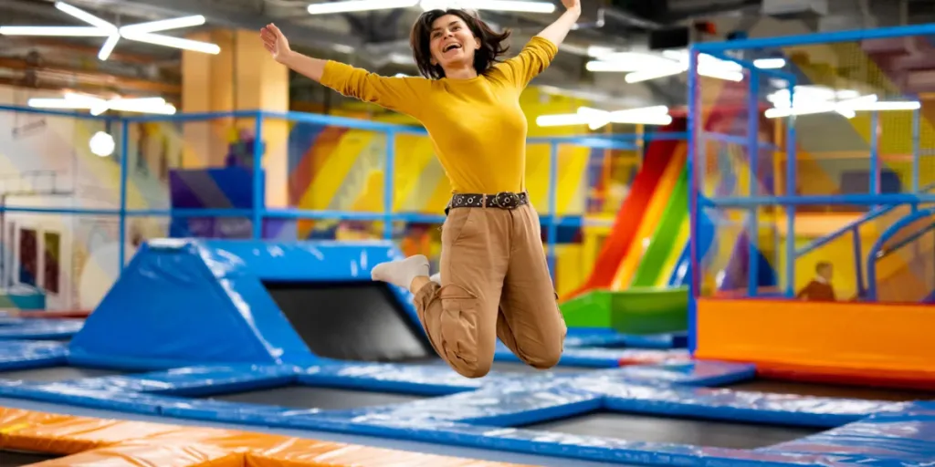 Pretty girl jumping on colorful trampoline at playground park and smiling.