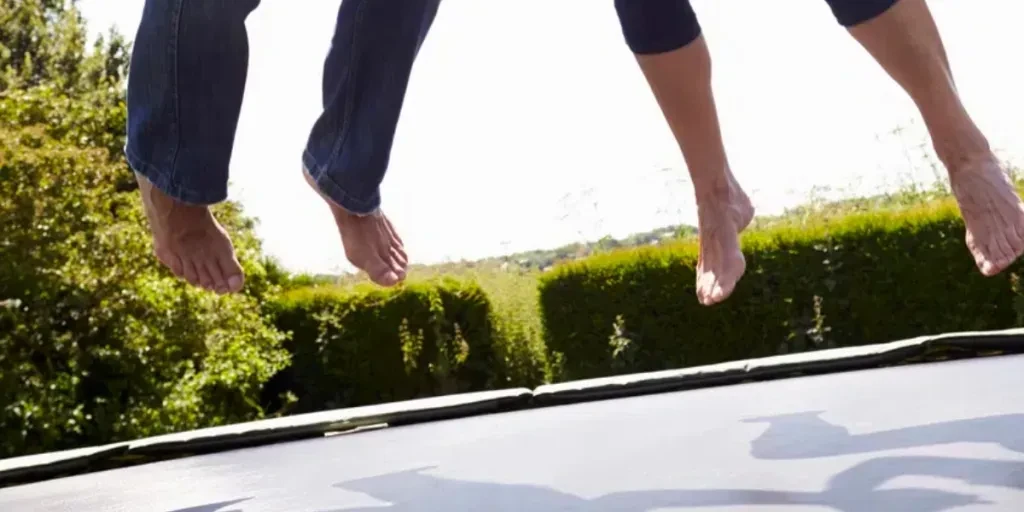 Senior Couple Bouncing On Trampoline In Garden Laughing