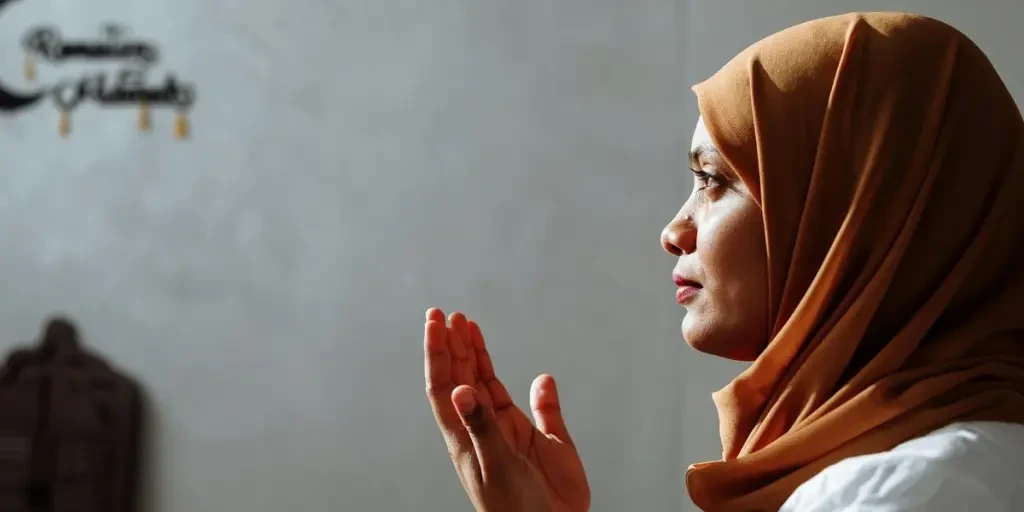 Side view of a Muslim woman in a brown hijab praying indoors with spiritual focus