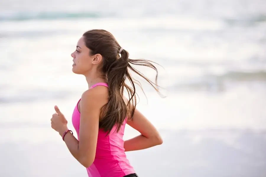 Side view of a young woman jogging on a beach wearing pink active wear