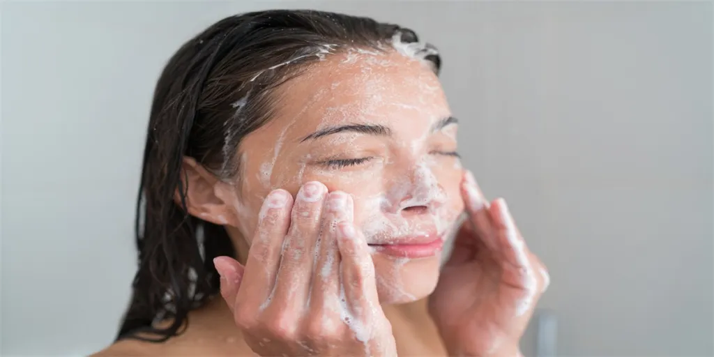 Skincare woman washing face in shower foaming facewash soap scrub on skin