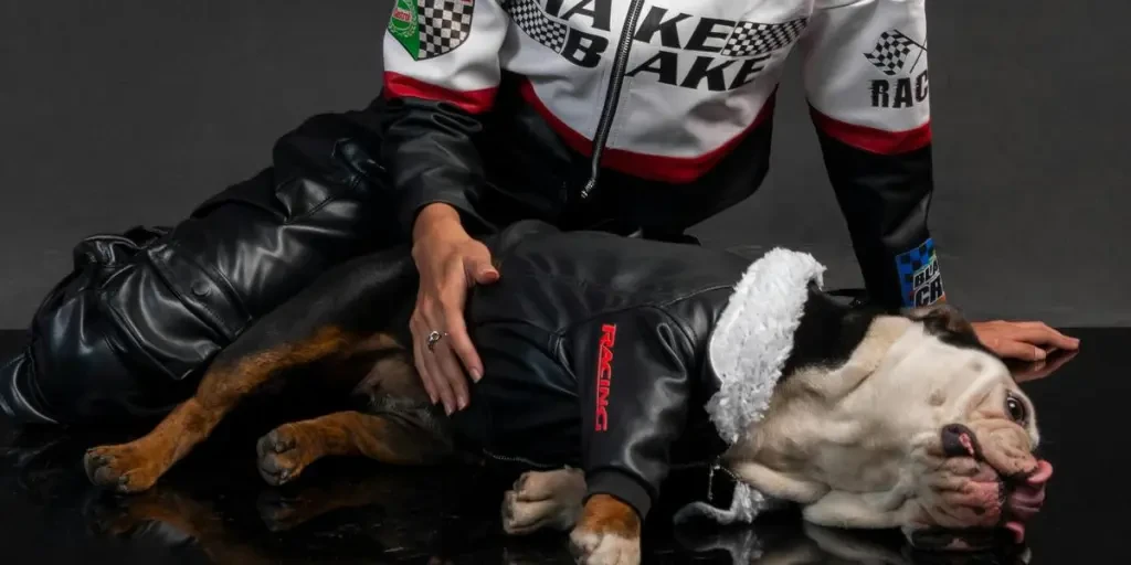 Smiling woman in a racing suit sitting with a bulldog on a reflective surface