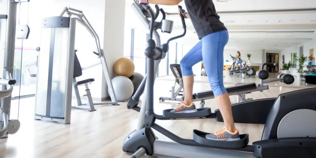 Smiling young attractive woman wearing sportswear and training on stair stepper in gym