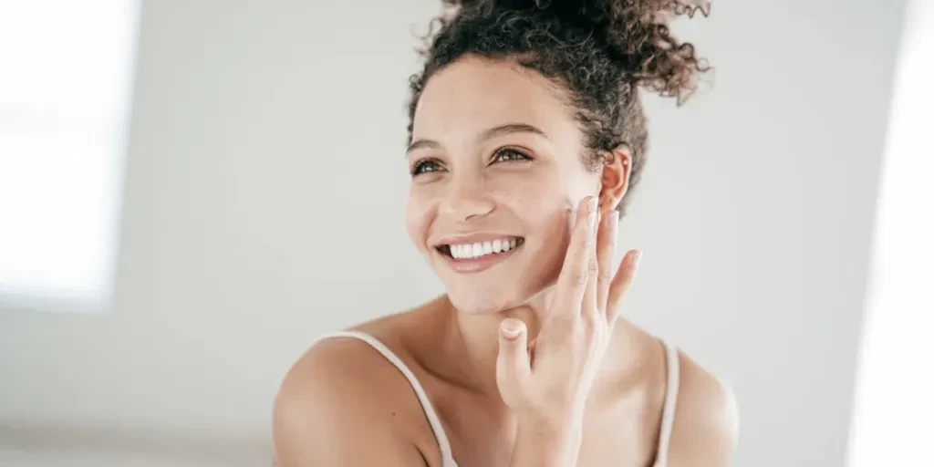 Smiling young women applying moisturiser to her face