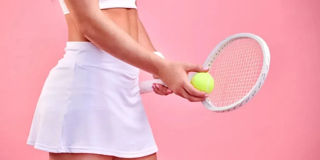 Studio shot of a sporty woman holding a tennis racket and ball against a pink background