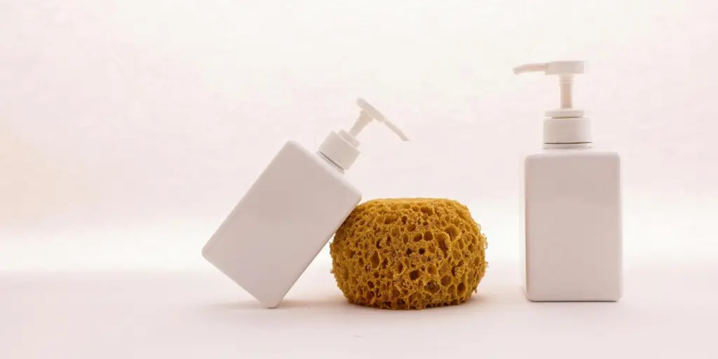 Stylish display of white cosmetic pump bottles and a yellow sponge on a clean white background, embodying minimalist bathroom aesthetics