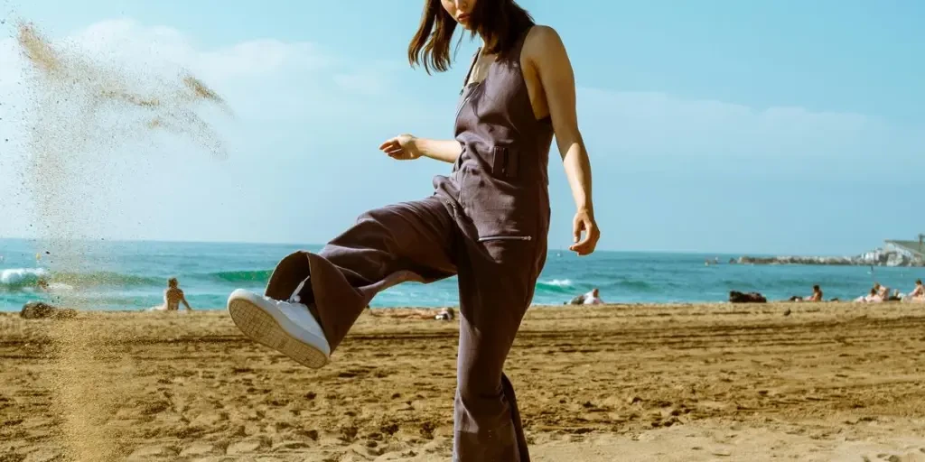 Stylish woman enjoying a sunny day at the beach, kicking sand playfully with the ocean in the background