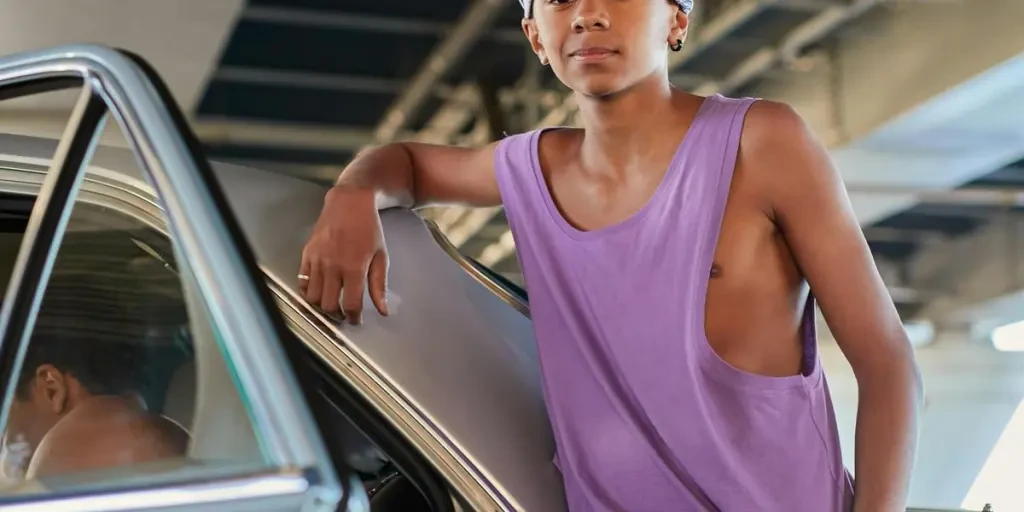 Stylish young man in streetwear leaning on car under urban bridge