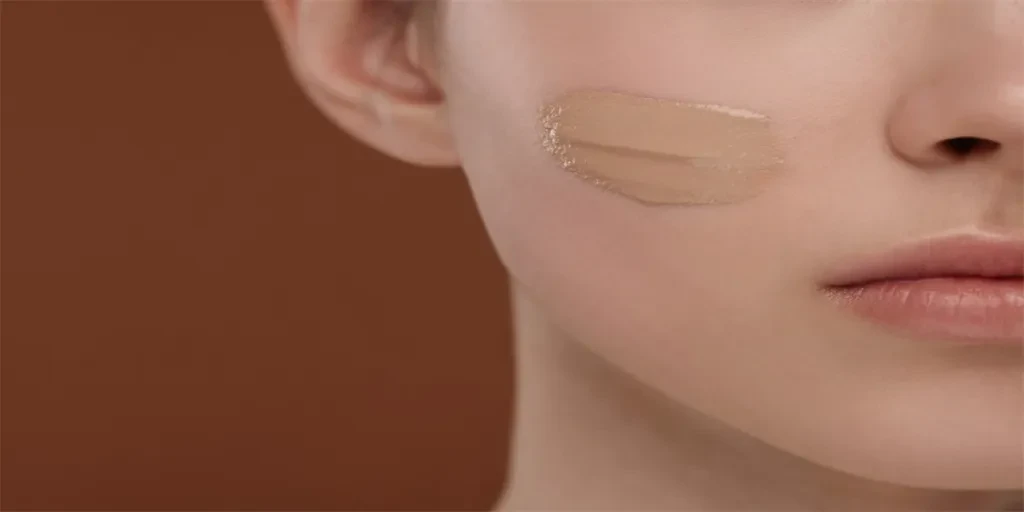 Teenage girl with swatch of foundation on face against brown background