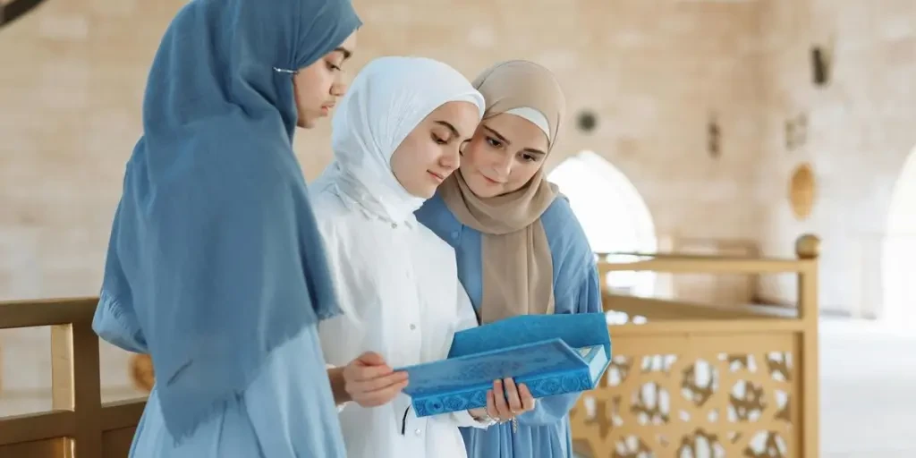 Three women in hijabs read the Quran together in a beautifully lit mosque interior