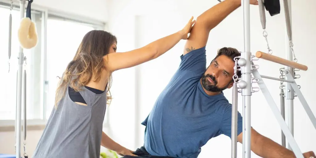 Trainer guides client on reformer machine during pilates session in a bright gym setting