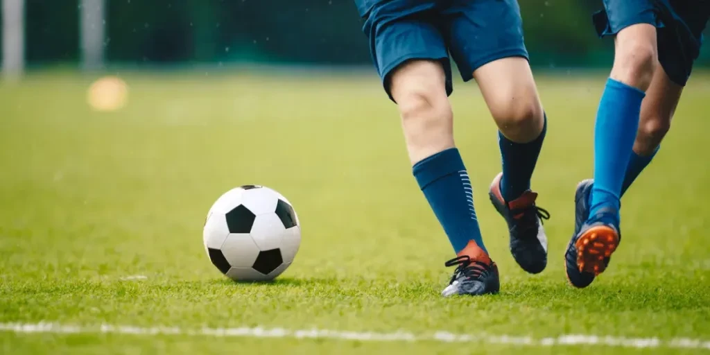 Two adult football players running and kicking a soccer ball