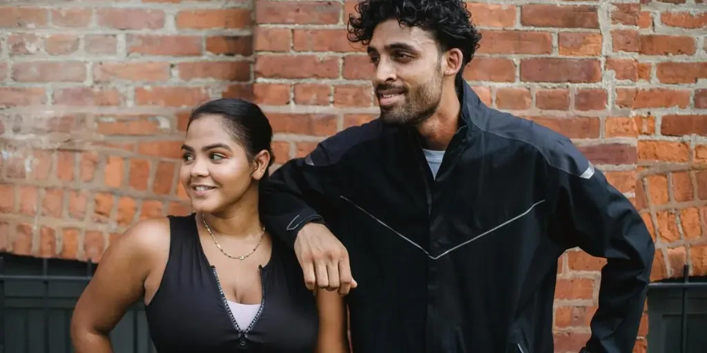 Two adults in sportswear smiling confidently against a brick wall. Embracing a healthy lifestyle