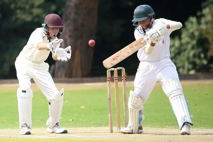 Two cricket players in action on a sunny day, showcasing skillful batting and wicket-keeping