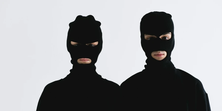 Two individuals wearing black balaclavas against a white background, highlighting anonymity and mystery