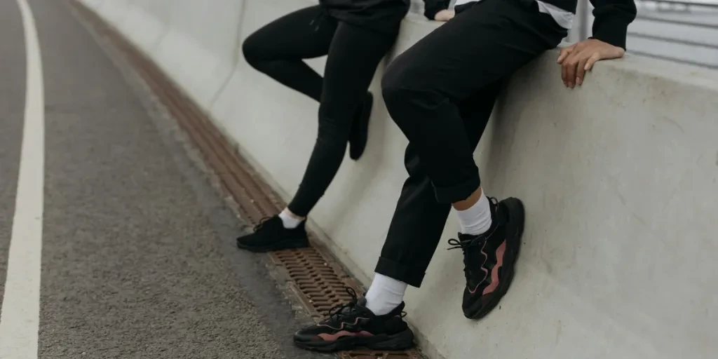 Two people in casual attire resting on a bridge barrier with sneakers and activewear