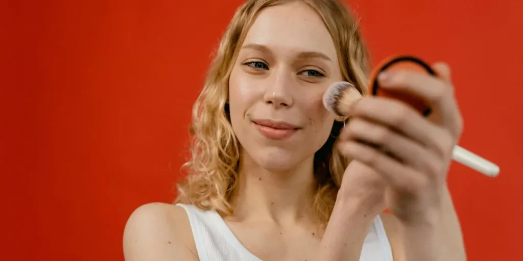 Woman applying makeup with a brush against a vibrant red backdrop, showcasing beauty and skincare concepts