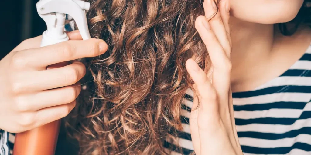 Woman applying spray on curly brown hair close-up