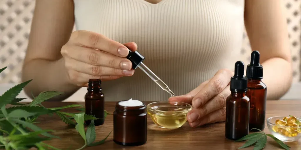 Woman dripping THC tincture or CBD oil into bowl at wooden table