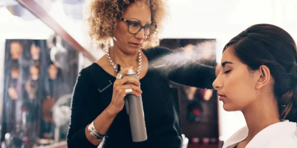 Woman hairdresser spraying hair setting liquid on her customer's hair