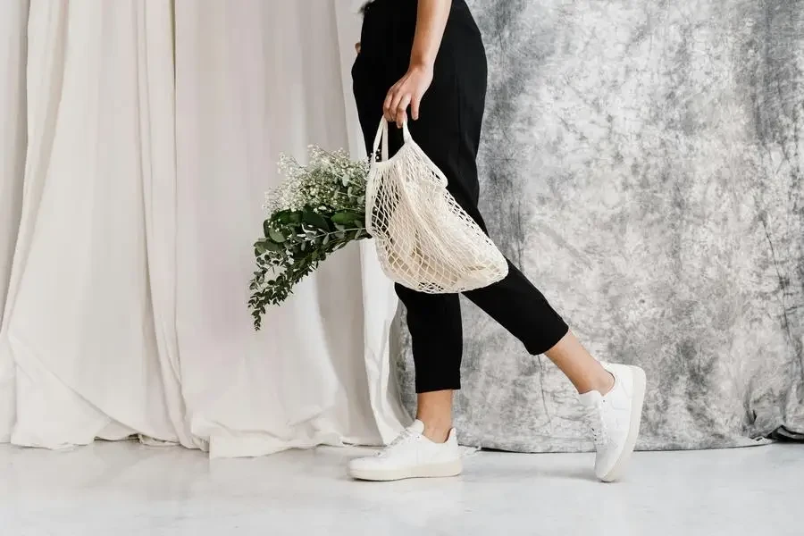 Woman in minimalist outfit holding an eco-friendly mesh bag filled with flowers, showcasing sustainable fashion