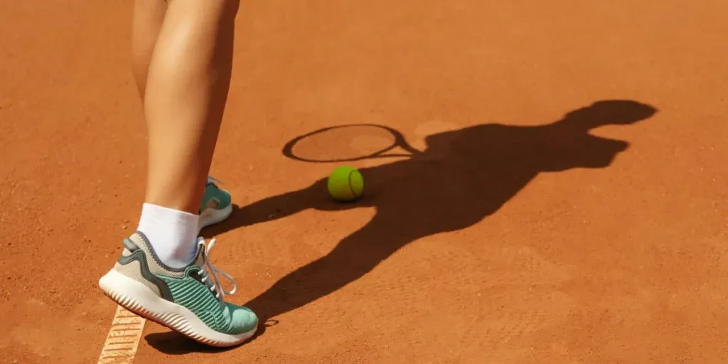 Woman in sneakers on clay court with tennis ball