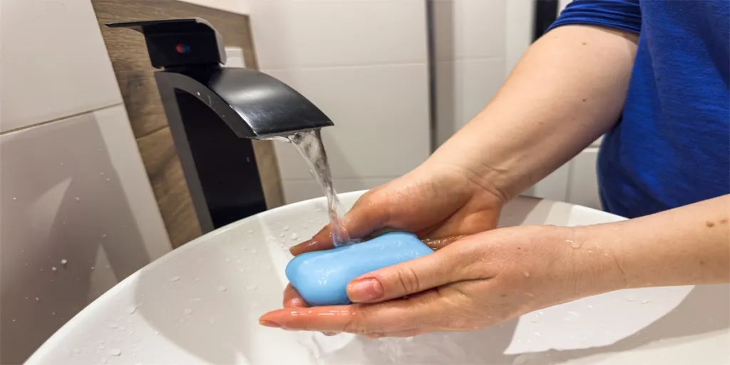 Woman washing hands under the faucet with soap in bathroom to prevent coronavirus infection