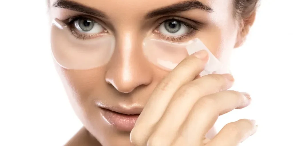 Woman with collagen pads under her eyes on white background