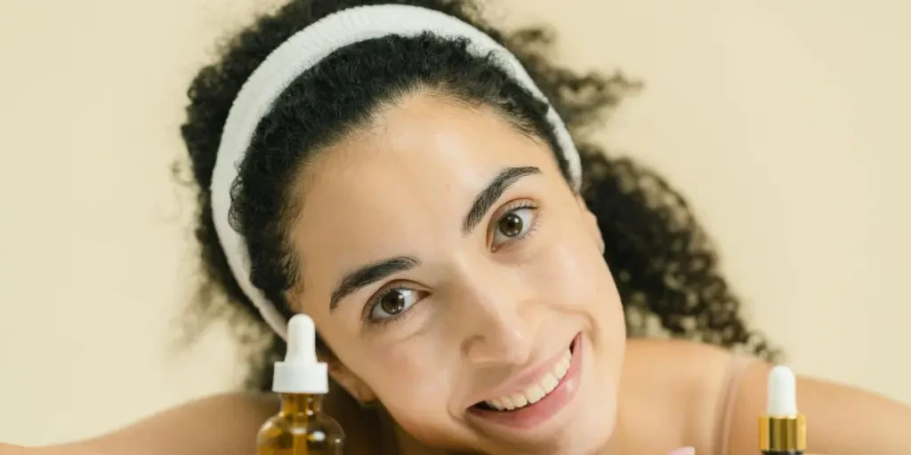 Woman with curly hair smiling, showcasing skincare products, indoors