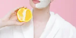 Woman with face mask holding orange halves against a pink background