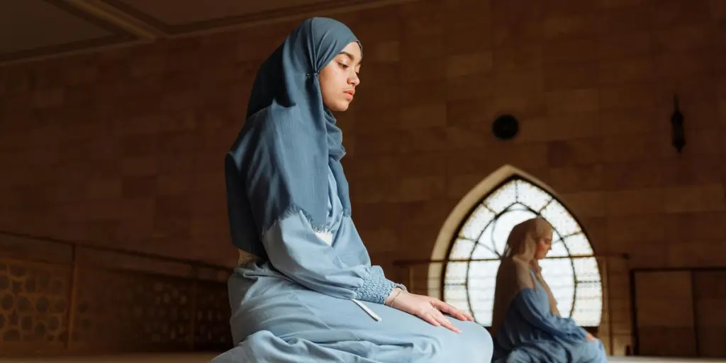 Women in hijab kneel in prayer inside a mosque, epitomizing devotion and tranquility