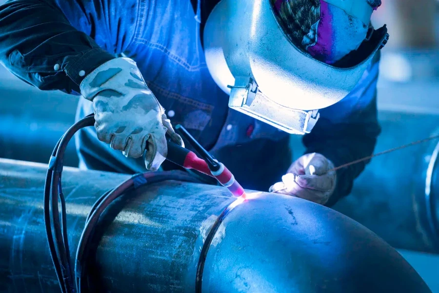 Worker welding metal piping using tig welder with protection