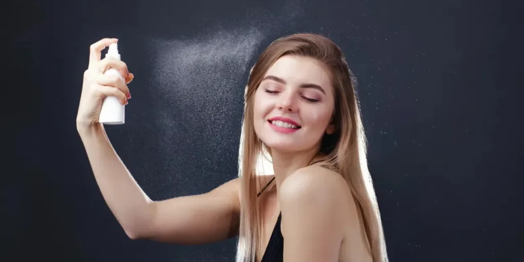 Young beautiful woman refreshing her face with termal water