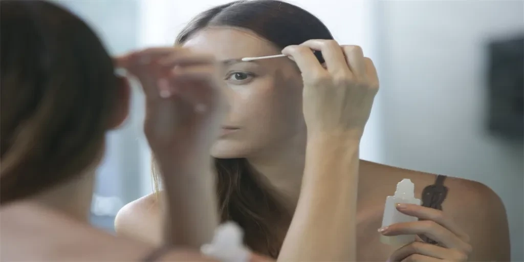 Young caucasian woman applying serum for eyebrows and eyelashes growth in front of the mirror