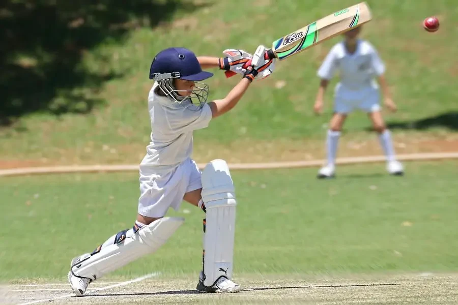Young cricketer in white gear executing a sweep shot on a sunny day