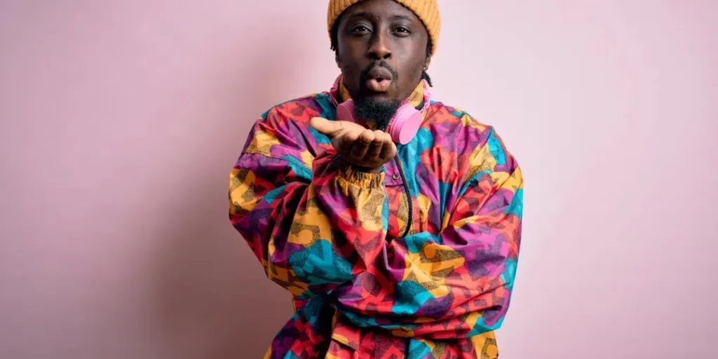 Young handsome african american man wearing colorful coat and cap over pink background looking at the camera