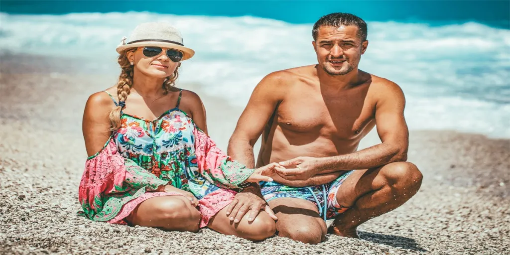 Young man and woman are posing on the sea beach in summer day and looking at camera