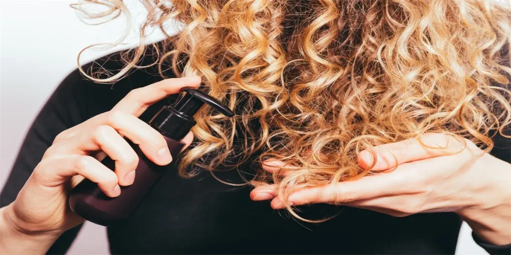 Young woman applying oil to her curly hair to prevent split ends