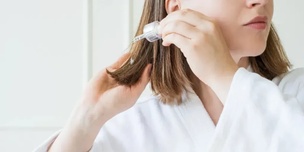 Young woman applying oil to her hair with a pipette on white background